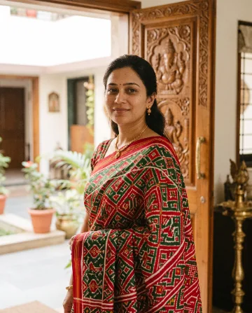 AI saree photo of the same woman in a red Patola silk saree with geometric patterns, beside a carved wooden door